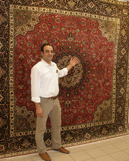 Parviz Moslemi steht vor einem Orientteppich.